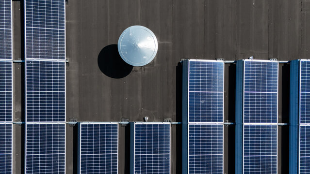 Aerial view of solar panels installed on a flat roof with a circular metallic vent in Mill, North Brabant, Netherlands.