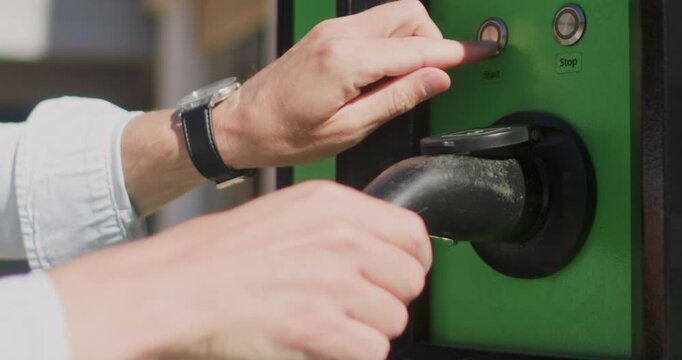Close-up of a man inserting a charging plug into a charging station and pressing the start button to begin charging an electric car.