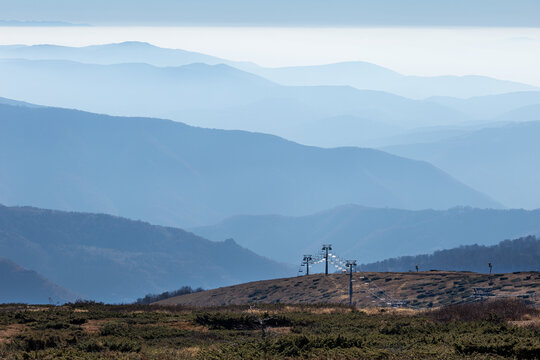 View of the Stara planina mountain range with a ski lift in the foreground and layers of hazy blue mountains in the distance in Babin zub, Pirot District, Serbia.