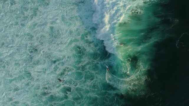 Cinematic aerial tracking of surfers in turquoise ocean water below Jaran Hill in Uluwatu Bali &ndash; Breathtaking bright daylight illuminating tropical sea surf lineup, commercial stock video 4k UHD asset