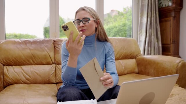 Woman talks on the phone while sitting on a couch in a bright room with a laptop and manila envelope 