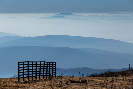View of Stara planina mountain range with layers of misty blue peaks and a wooden fence in the foreground at Babin zub, Pirot District, Serbia.