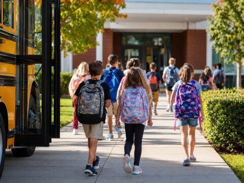 Diverse Elementary School Students with Backpacks Walking Toward School Building Near Yellow Bus for Back to School Education Concept