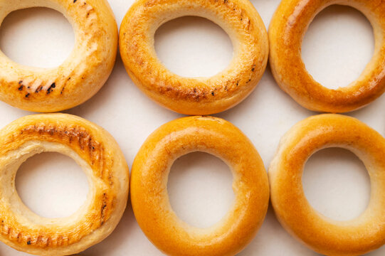 Fresh bagels form close-up food composition on pale background. Ring pastries with golden crust and baked texture suit bakery promotion, snack campaigns, breakfast menus and commercial food design.