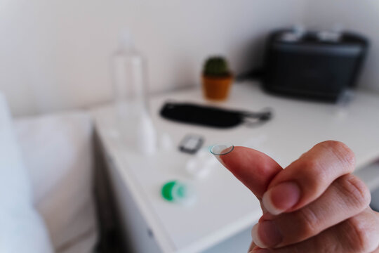 Orthokeratology night lens held on a fingertip with lens case and eye care supplies. Overnight corneal reshaping supports myopia control and daytime vision