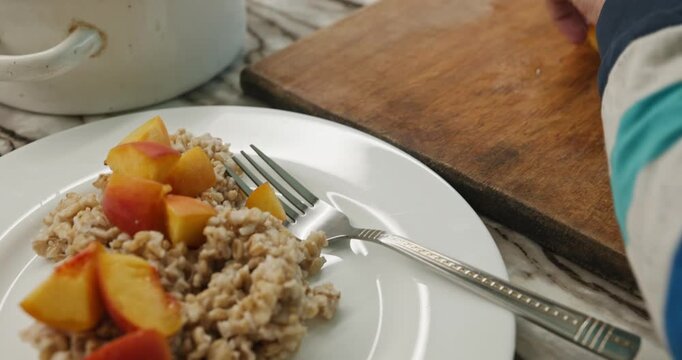 Caucasian kid boy put on dish oatmeal and peach. Child preparing food. 4K 10-bit