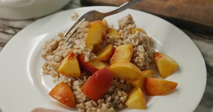 Caucasian kid boy put on dish oatmeal and peach. Child preparing food. 4K 10-bit
