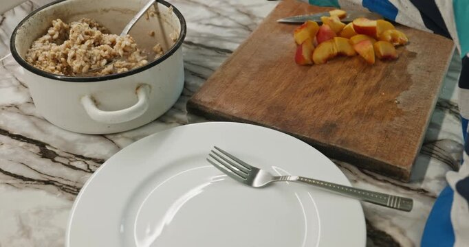 Caucasian kid boy put on dish oatmeal and peach. Child preparing food. 4K 10-bit