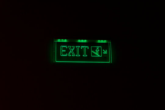 Bright green exit sign glowing in darkness, featuring a running figure and arrow indicating the way out. Ideal for emergency, safety, and direction concepts.