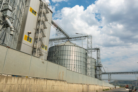Large metal silos and industrial buildings under a partly cloudy sky, showcasing modern architecture and manufacturing infrastructure.