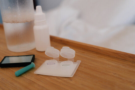 Orthokeratology lens cases, contact lenses and insertion tool arranged on a wooden surface. Orthokeratology therapy treats myopia through overnight corneal reshaping and supports myopia control.