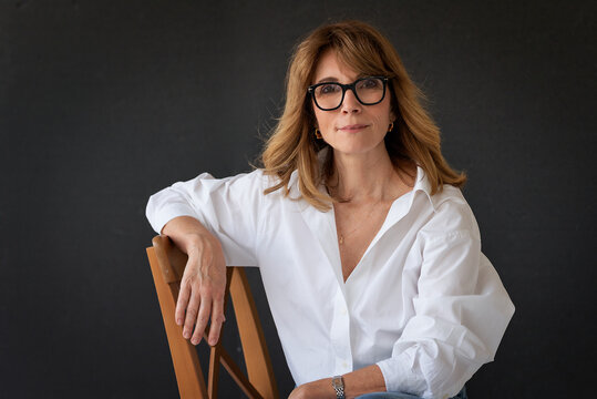 Blond haired woman wearing glasses and white shirt against isolated dark background