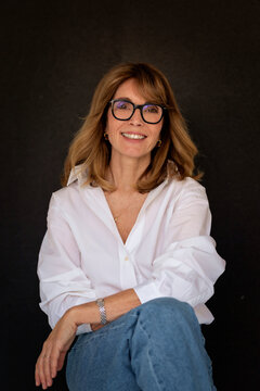 Blond haired woman wearing glasses and white shirt against isolated dark background