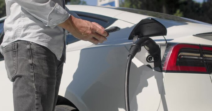 Driver takes his smartphone out of the back pocket of his jeans and sets up the charging of his electric plane.