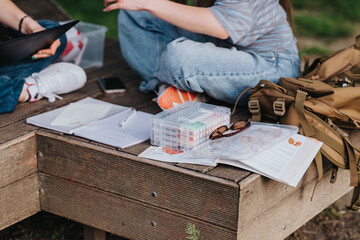 Obraz na płótnie Canvas Student sitting on a wooden bench with open notebooks, art supplies and a backpack. The scene shows casual outdoor studying and creative work in a park setting.