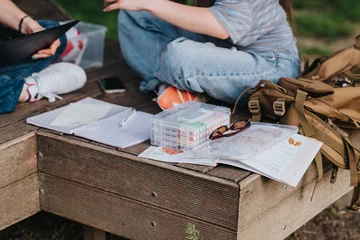 Fotobehang Sportwinkel Student sitting on a wooden bench with open notebooks, art supplies and a backpack. The scene shows casual outdoor studying and creative work in a park setting.  © qunica.com