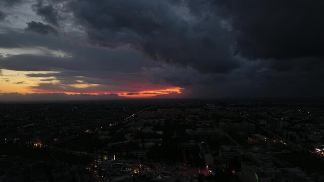 Aerial drone view of an urban landscape in Syria at sunset. City skyline and street lights during dusk. Middle Eastern city view under colorful evening clouds.
