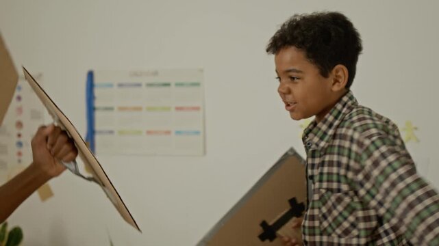 Two African American boys playing with homemade cardboard swords and shields in bedroom. Clip is ideal for family lifestyle commercials, creative play promotions, or parenting campaigns