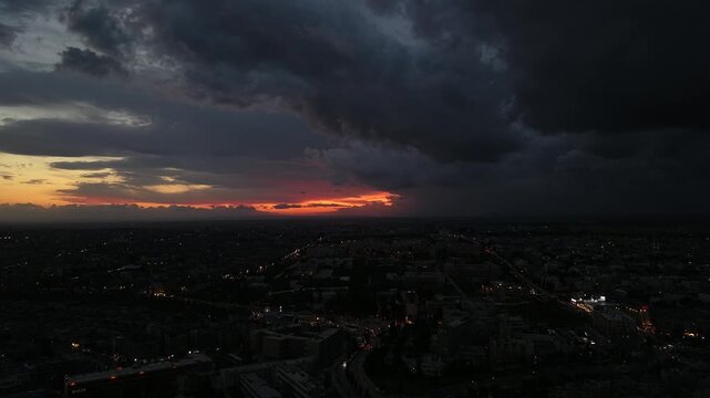 Aerial drone view of an urban landscape in Syria at sunset. City skyline and street lights during dusk. Middle Eastern city view under colorful evening clouds.