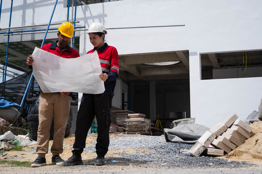 Construction engineers reviewing architectural blueprints at an active building site, ensuring project planning, structural inspection, quality control, workplace safety, and construction management.