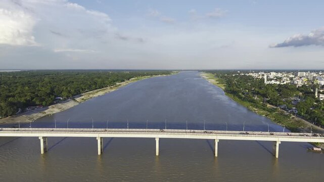 Aerial drone footage showing Haripur Bridge crossing the Gorai River in Kushtia, Bangladesh, with the wide river, green riverbanks, and city buildings visible in the distance.