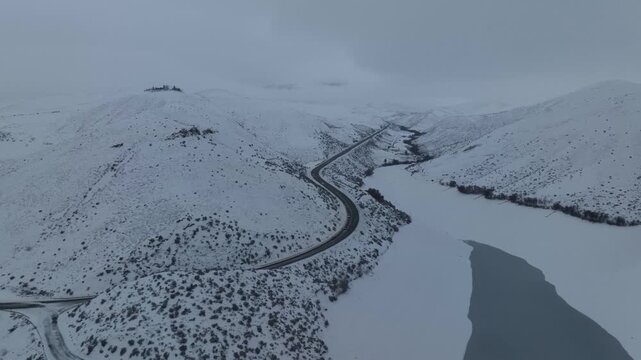 Aerial view of Lucky Peak Lake and winding road surrounded by snow-covered hills in Ada County, Idaho, United States.