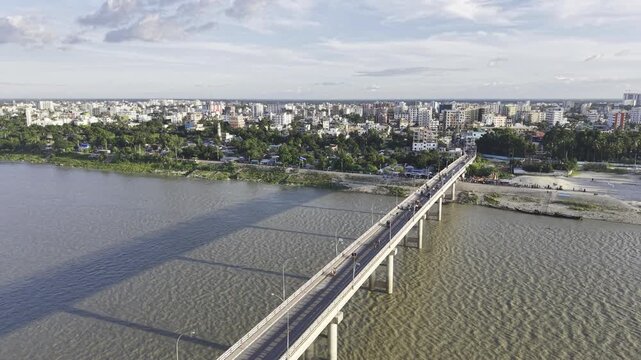 Drone flying backward along Haripur Bridge over the Gorai River, revealing the surrounding riverbanks, urban buildings, and city landscape of Kushtia, Bangladesh.