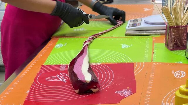 Twisted burgundy candy rope rests on mats near digital scale, scissors and bundle of wooden sticks in confectionery workshop.