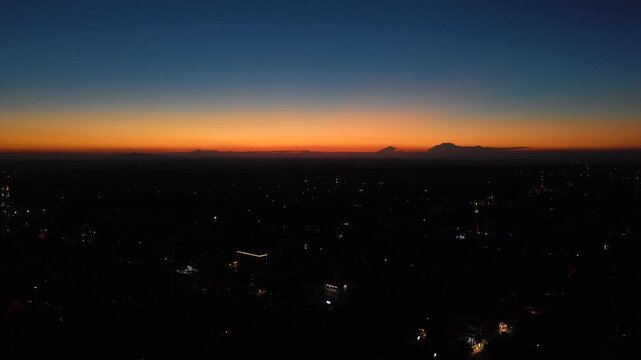 Aerial drone view of an urban landscape in Syria at sunset. City skyline and street lights during dusk. Middle Eastern city view under colorful evening clouds.