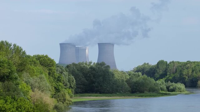 A nuclear power plant with large cooling towers emitting steam, situated behind a lush green forest and next to a calm river, wide shot.