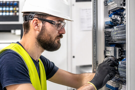 A male technician wearing a hard hat and safety glasses is working on server racks in a data center or server room.
