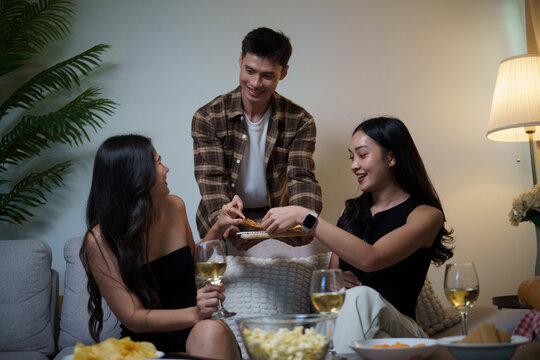 Young Asian man serving snacks to female friends during a home gathering.