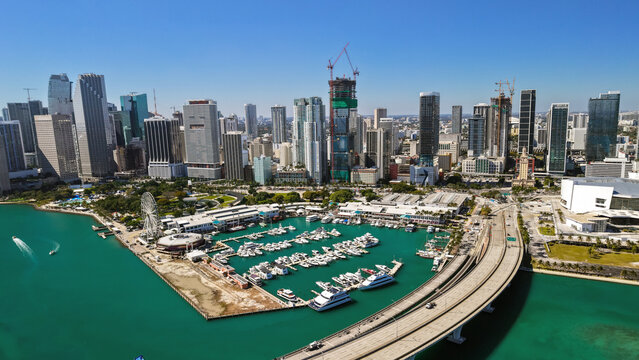 Aerial view of the Miami skyline featuring Bayside Marketplace, a marina with yachts, and surrounding urban architecture under a clear blue sky in Miami, Florida, United States.