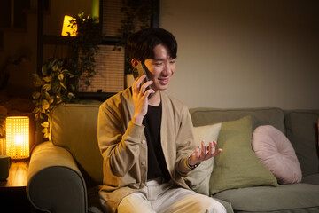 Fototapeta premium Young Asian man talking on a smartphone while relaxing at home.