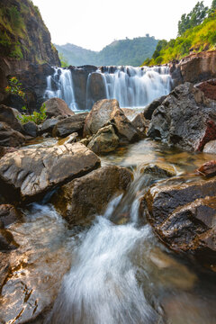 View of the waterfall cascading over dark rocks into a flowing stream surrounded by lush greenery in Karad, Maharashtra, India.