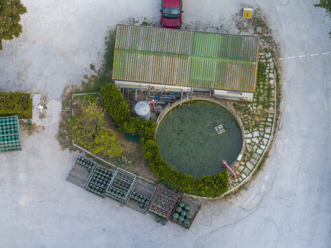 Aerial view of a circular water reservoir next to a small industrial building with a green roof, surrounded by storage racks of gas cylinders in Fermo, Marche, Italy.