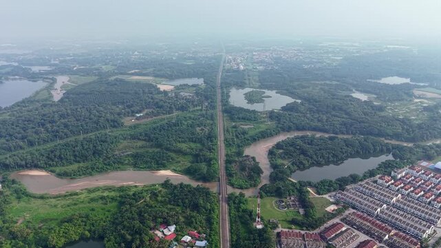 Aerial drone panorama of abandoned tin mining lakes, railway corridor, wetlands and suburban development under hazy sky at Kampar, Perak