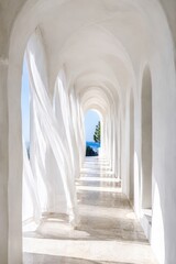 Fototapeta premium White arched corridor with sheer curtains at seaside villa