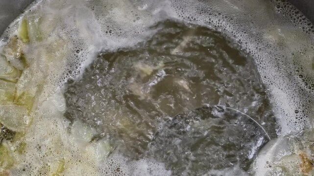 Close up of chicken broth boiling in a large pot at a traditional Vietnamese chicken rice restaurant