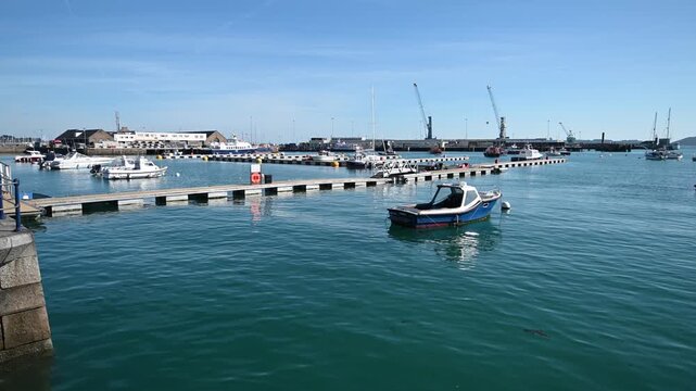 St Peter Port Harbour,Guernsey Channel Islands.Water level view of small boat bobbing in the harbour looking over pontoons to Cambridge Berth and docks swinging around to harbour entrance