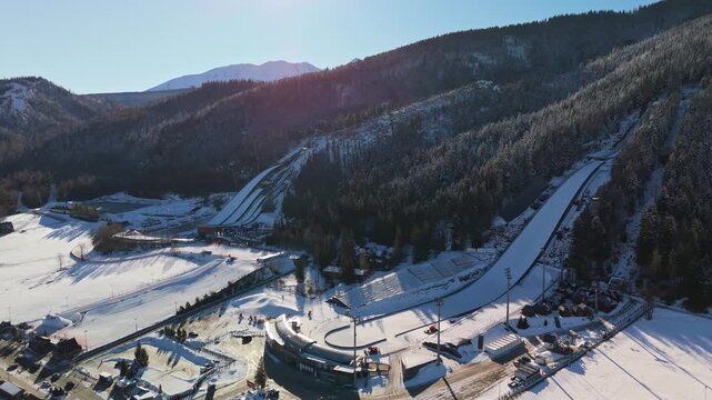 Aerial view of Wielka Krokiew ski jumping stadium in Zakopane, Poland, surrounded by snowy slopes, evergreen forest and the Tatra Mountains under a clear winter sky.
