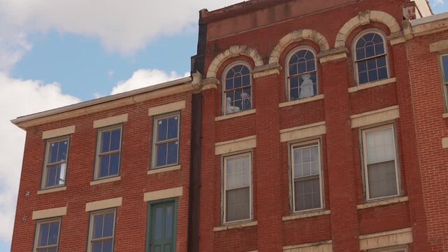 Historic red brick building facade with arched upper windows and mannequins inside on a bright daytime sky.