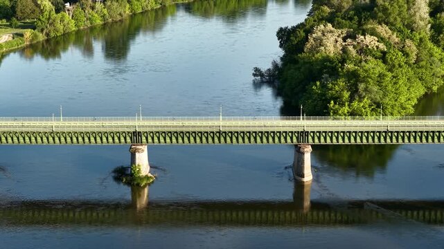 The historic Pont Canal de Briare in Briare, France, showing the iconic aqueduct bridge spanning a wide river with lush green trees along the riverbanks, aerial view.