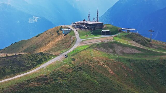 Aerial view of a car ascending a scenic road to the doss del sabion mountain peak, showing a mountain refuge and the brenta dolomites