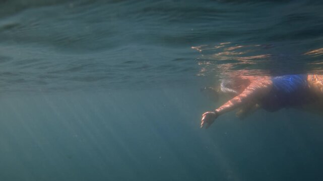 Person wearing a snorkel mask, swimming underwater in clear blue ocean with sunbeams penetrating the surface