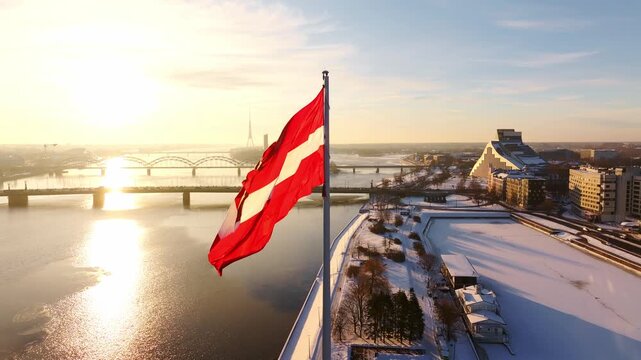 Latvian flag waves above snowy Riga as sunrise glows across Daugava River water