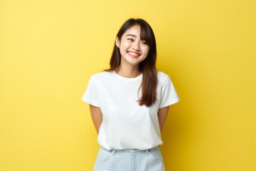 Obraz premium Happy young woman standing against yellow studio background, looking cheerful