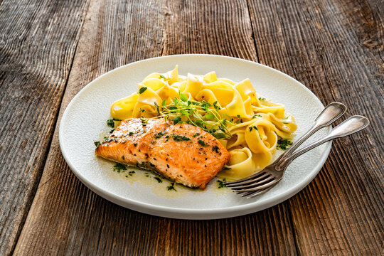Pasta with baked salmon steak on wooden table
