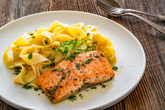 Pasta with baked salmon steak on wooden table
