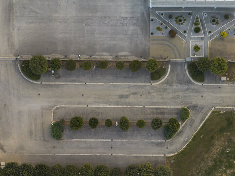 Aerial view of a parking lot with rows of trees, paved surfaces, and geometric landscaping in Fermo, Marche, Italy.